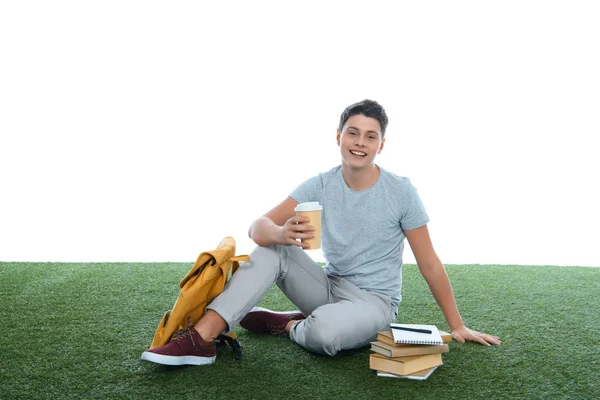 Adolescente studente ragazzo seduto su erba con caffè per andare isolato su bianco — Foto stock