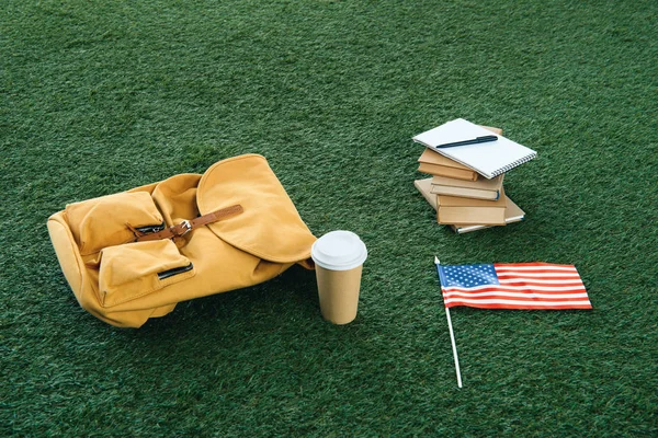 Mochila amarela vintage e material escolar com bandeira dos EUA na grama verde — Fotografia de Stock