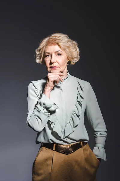 Thoughtful senior woman in stylish shirt looking at camera on dark grey — Stock Photo