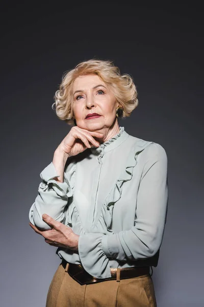Pensativa mujer mayor mirando hacia arriba en gris oscuro - foto de stock