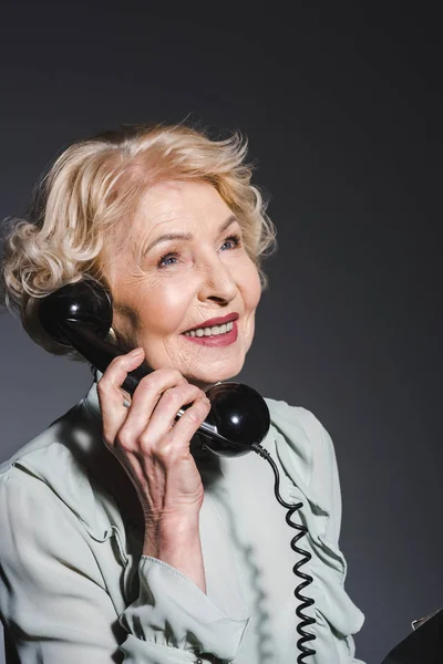 Nahaufnahme Porträt einer lächelnden Seniorin, die mit einem Oldtimer-Telefon auf dunkelgrau spricht — Stockfoto