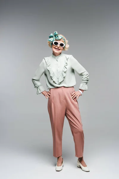 Séduisante femme âgée en bandeau élégant et lunettes de soleil sur gris — Photo de stock