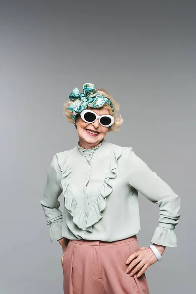 Felice donna anziana in fascia elegante e occhiali da sole isolati su grigio — Foto stock