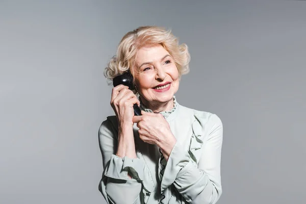 Close-up portrait of smiling senior woman talking by vintage phone isolated on grey — Stock Photo