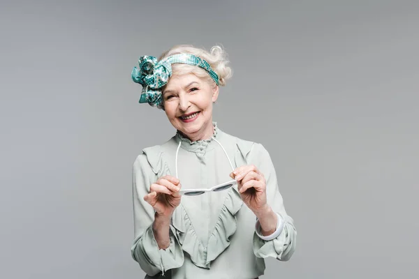 Happy senior woman in stylish vintage clothes and sunglasses isolated on grey — Stock Photo