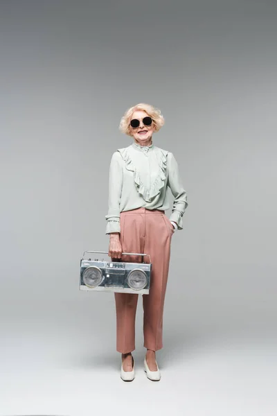 Schöne Seniorin in stylischer Sonnenbrille mit Vintage-Boombox auf grau — Stockfoto