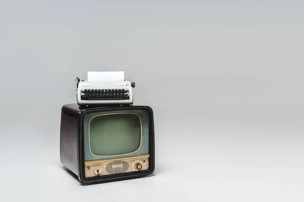 Вінтажний телевізор з друкарською машинкою зверху на сірій поверхні — стокове фото