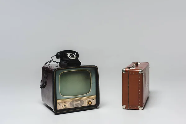 Vintage tv with rotary phone and suitcase on grey — Stock Photo