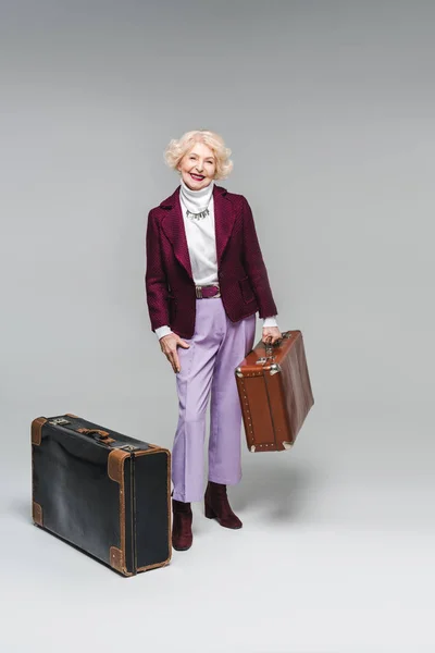 Lächelnde Seniorin mit Vintage-Koffern auf grau — Stockfoto