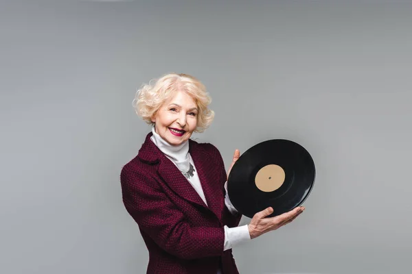 Happy senior woman holding vinyl disc isolated on grey — Stock Photo