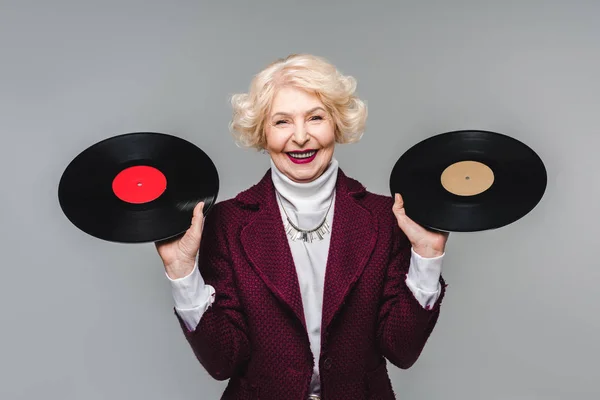 Happy stylish senior woman holding vinyl discs isolated on gray background — Stock Photo