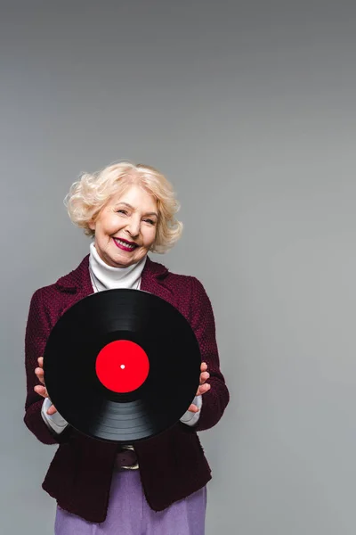 Elegante donna anziana sorridente che tiene il disco in vinile isolato su sfondo grigio — Foto stock