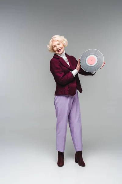 Feliz elegante mulher sênior segurando disco de vinil no fundo cinza — Fotografia de Stock