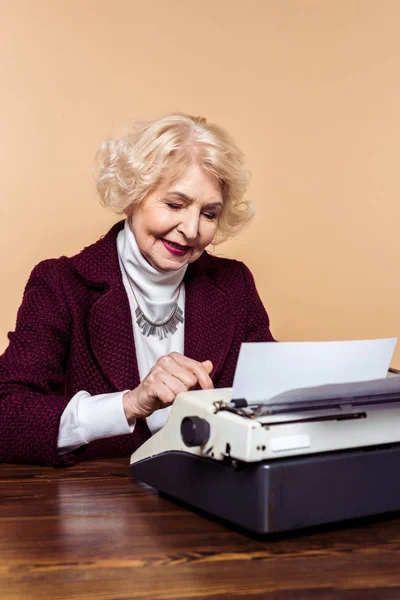 Femme âgée à la mode en utilisant la machine à écrire à la table — Photo de stock