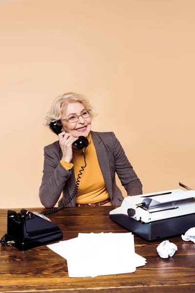 Donna anziana elegante sorridente in occhiali da vista che parla a telefono rotante a tavola — Foto stock