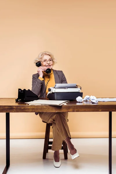 Donna anziana elegante sorridente che parla a tavola al telefono rotante — Foto stock