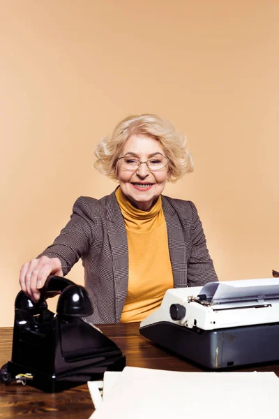 Mujer mayor con estilo que pone el teléfono rotativo en la mesa con la máquina de escribir - foto de stock