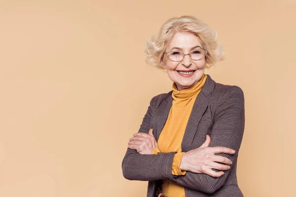 Sorridente donna anziana alla moda in occhiali posa isolata su sfondo beige — Foto stock