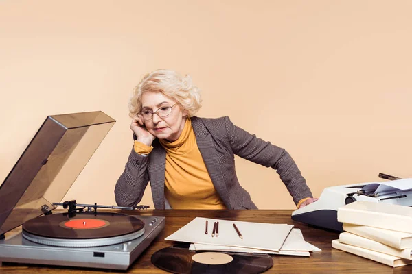 Upset senior woman listening vinyl record player at table — Stock Photo