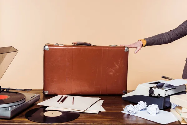 Tiro recortado de mão feminina segurando na mala vintage na mesa com máquina de escrever, disco de vinil e gravador — Fotografia de Stock