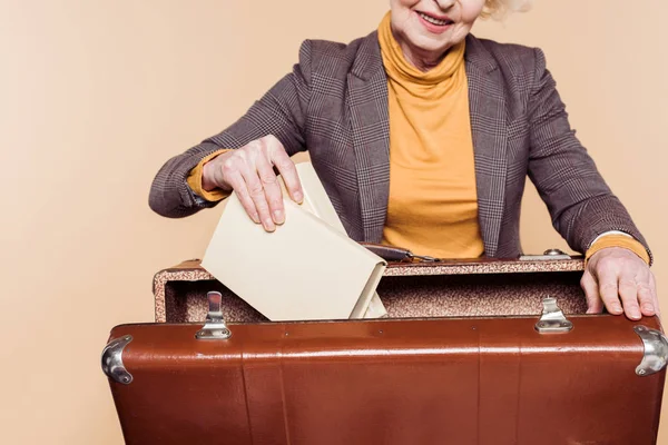 Recortado tiro de la mujer mayor con estilo poner libros en la maleta vintage - foto de stock