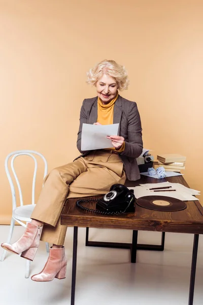 Élégant femme âgée écriture en papier et assis sur la table avec téléphone rotatif et disque de vinyle — Photo de stock