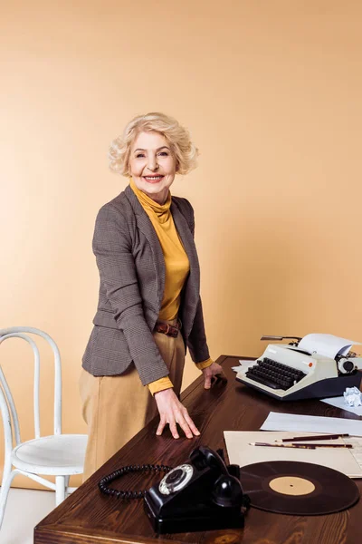 Élégante femme âgée debout à la table avec téléphone rotatif, plaque de vinyle et machine à écrire — Photo de stock