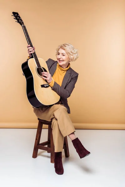 Stylish senior woman sitting on chair and playing on acoustic guitar — Stock Photo