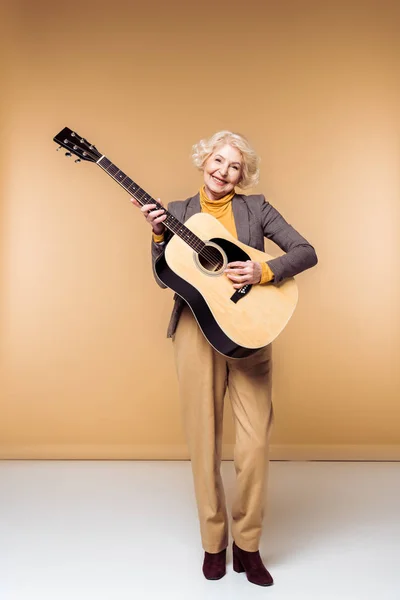 Smiling stylish senior woman playing on acoustic guitar — Stock Photo