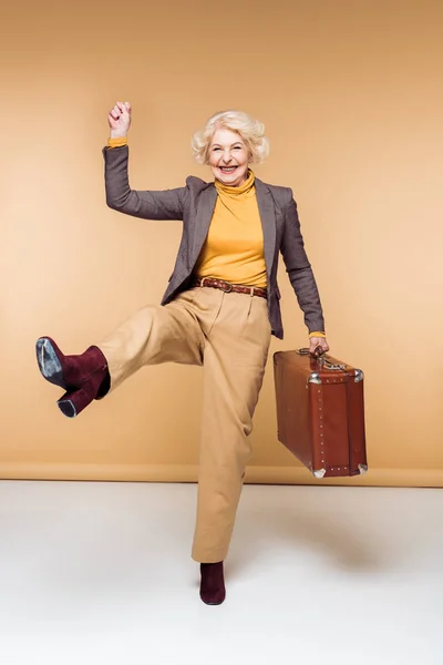 Elegante viaggiatore femminile anziano eccitato con braccio sollevato tenendo valigia vintage — Foto stock