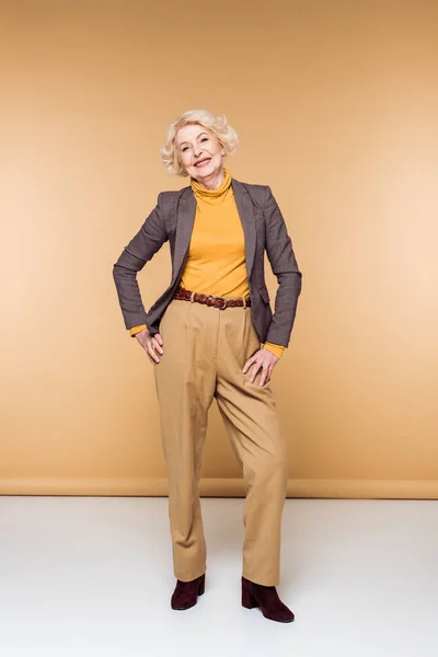 Souriant femme âgée à la mode posant sur beige — Photo de stock