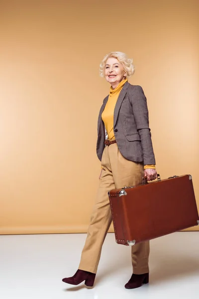 Stylish senior female traveler holding vintage suitcase — Stock Photo