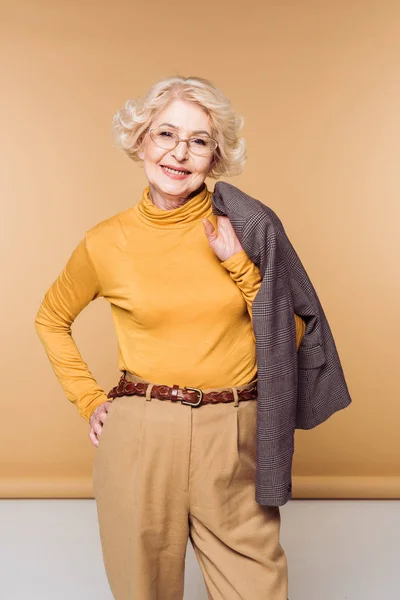 Smiling stylish senior woman in eyeglasses holding jacket on shoulder — Stock Photo
