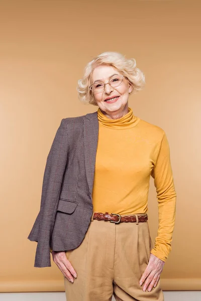 Happy fashionable senior woman in eyeglasses holding jacket on shoulder — Stock Photo