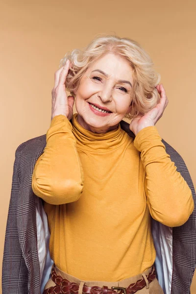 Senior woman with jacket on shoulders adjusting haircut isolated on beige background — Stock Photo