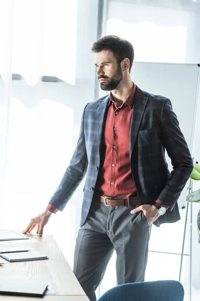 Schöner junger Geschäftsmann, der neben seinem Arbeitsplatz im Büro steht — Stockfoto