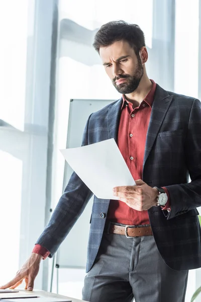 Handsome young businessman in stylish suit reading business document — Stock Photo