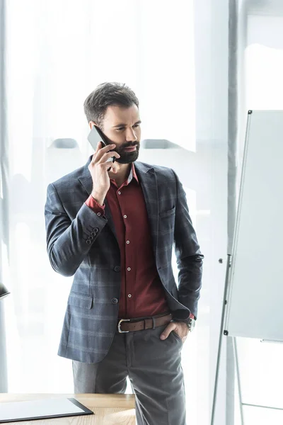 Handsome young businessman in stylish suit talking by phone at office — Stock Photo