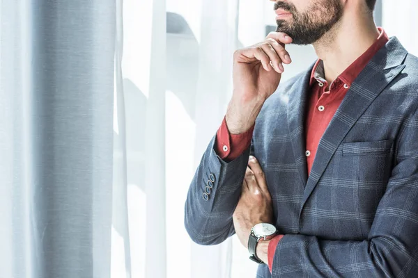 Schnappschuss eines jungen Geschäftsmannes mit Hand am Kinn, der durch das Fenster schaut — Stockfoto