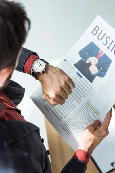 High angle view of businessman reading newspaper and looking at watch at office — Stock Photo