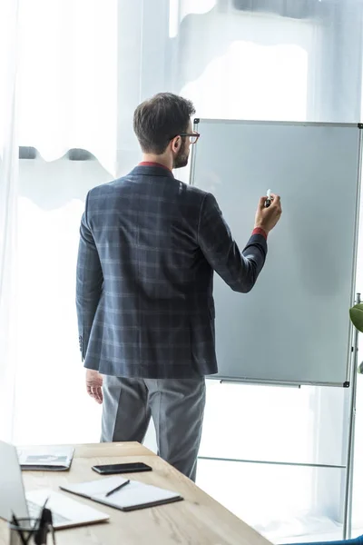 Vue arrière du jeune homme d'affaires écrivant sur tableau blanc vierge — Photo de stock