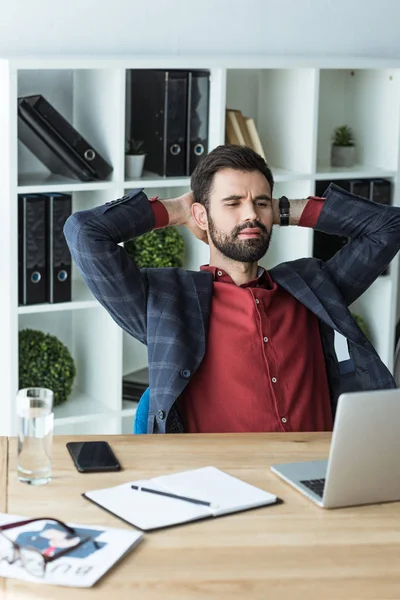 Beau jeune homme d'affaires relaxant sur le lieu de travail avec les mains derrière la tête — Photo de stock