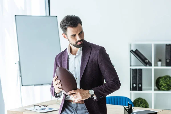 Schöner junger Geschäftsmann mit American Football Ball im Büro — Stockfoto