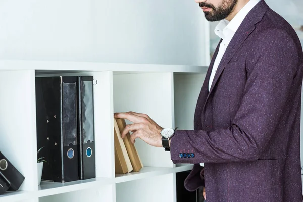 Cropped shot of businessman taking book from shelf at office — Stock Photo