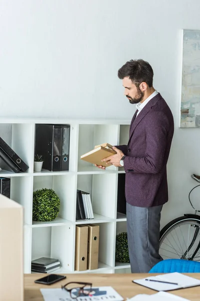 Schöner junger Geschäftsmann stellt Bücher im Büro ins Regal — Stockfoto