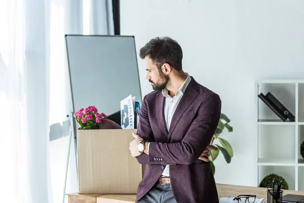 Despedido joven empresario mirando a la caja de cosas personales en la oficina - foto de stock