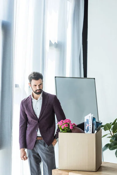 Schöner junger Geschäftsmann schaut auf Schachtel mit persönlichen Sachen im Büro — Stockfoto