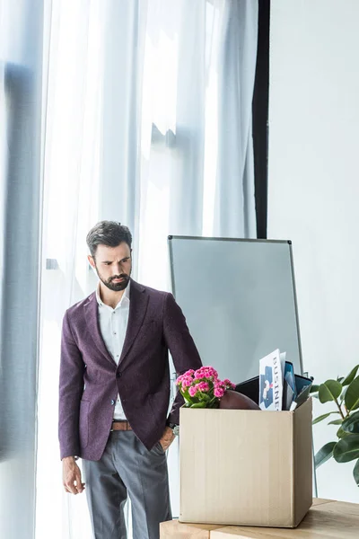 Joven hombre de negocios guapo mirando la caja de cosas personales en la oficina - foto de stock