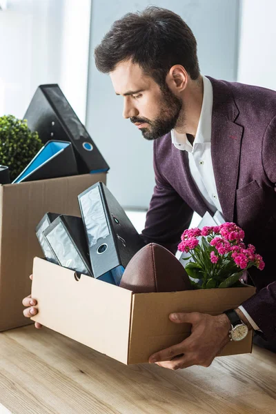 Despedido joven empresario tomando caja de cosas personales de escritorio en la oficina - foto de stock