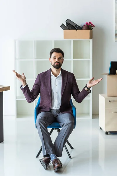 Bewildered young businessman sitting on chair in office after he gets fired — Stock Photo